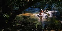 Un niño juega sentado en una piedra del cauce del río Arrago.