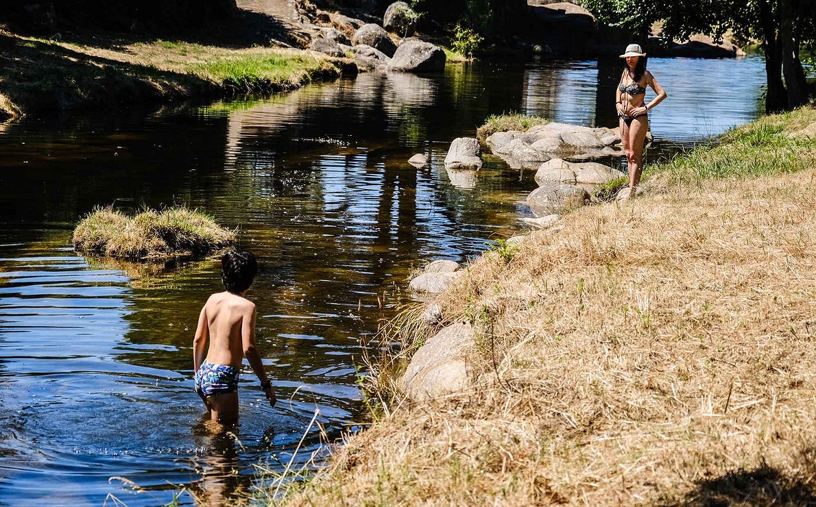 Una mujer en la orilla del río Arrago observa a un niño metido en el agua, en Cadalso.