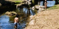 Una mujer en la orilla del río Arrago observa a un niño metido en el agua, en Cadalso.