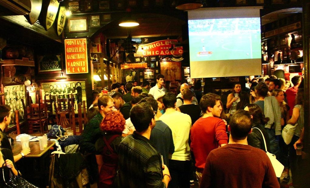 Bar lleno de gente con una pantalla y un partido proyectado.